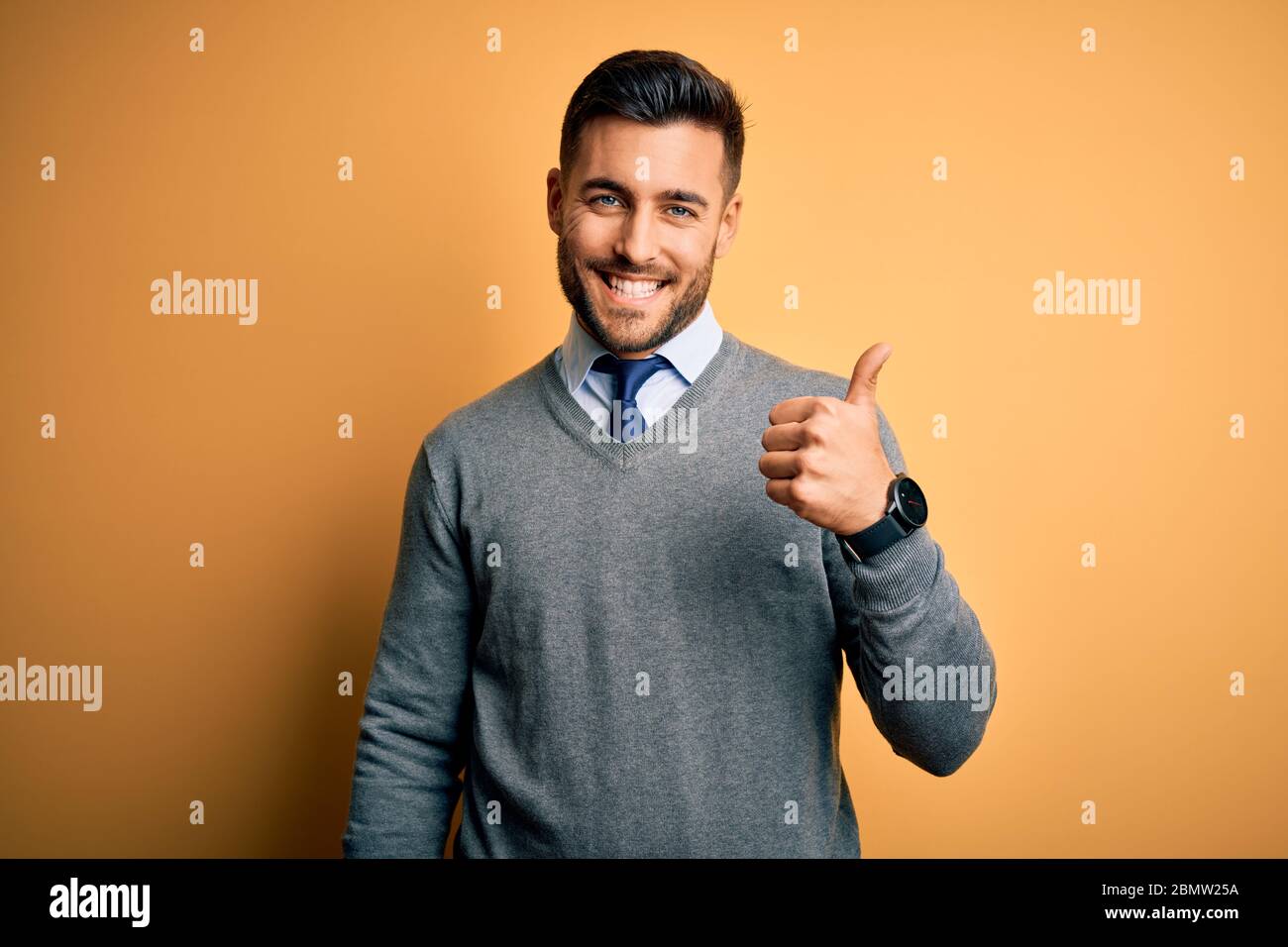 Joven hombre de negocios guapo con elegante Jersey y corbata sobre fondo  amarillo haciendo feliz pulgares hasta gesto con la mano. Aprobación de la  expresión Lookin Fotografía de stock - Alamy