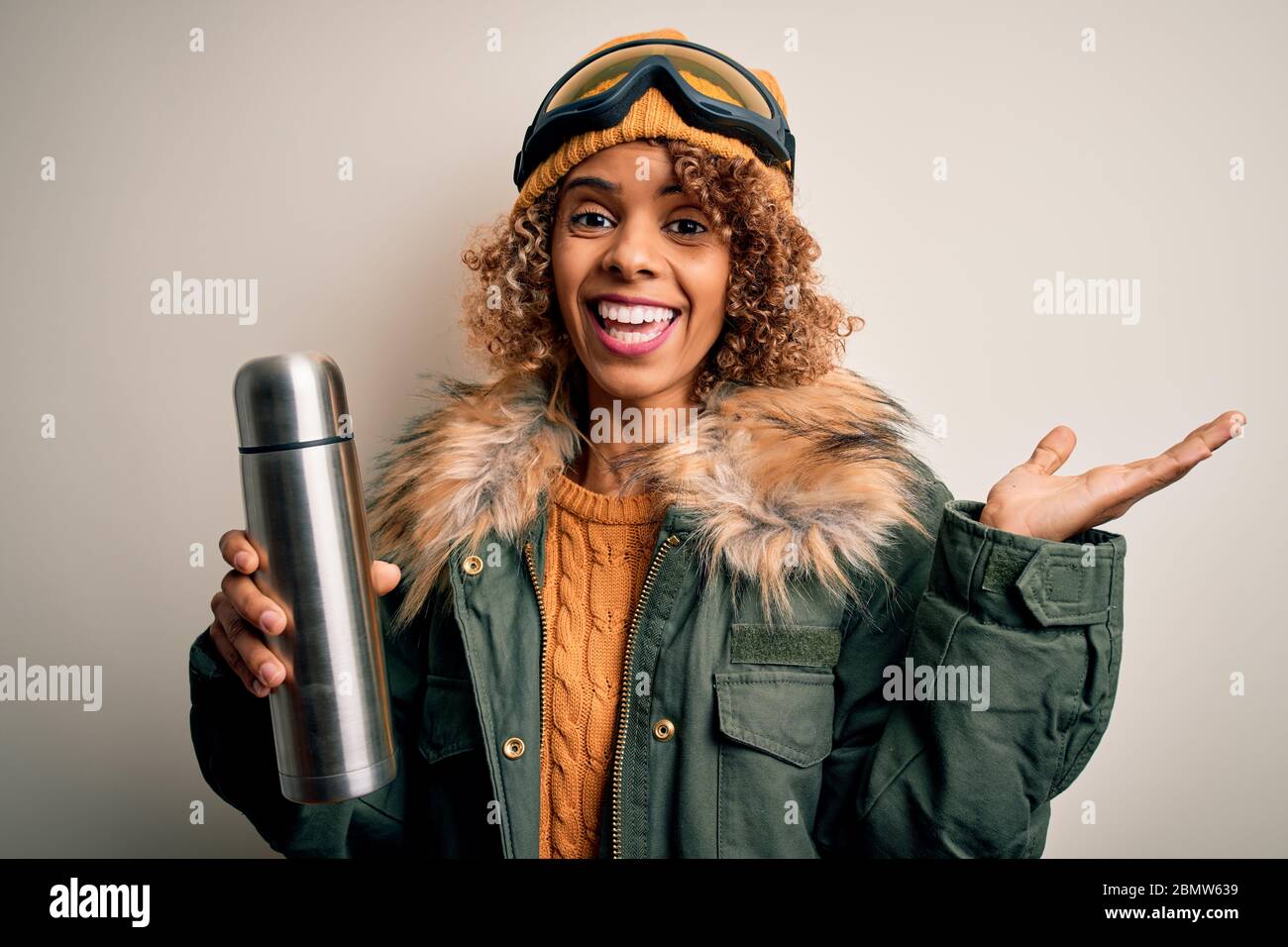 Joven afroamericana esquiadora con gafas de esquí tomando termo con café muy feliz y emocionado, la expresión ganadora celebrando la victoria grito Foto de stock