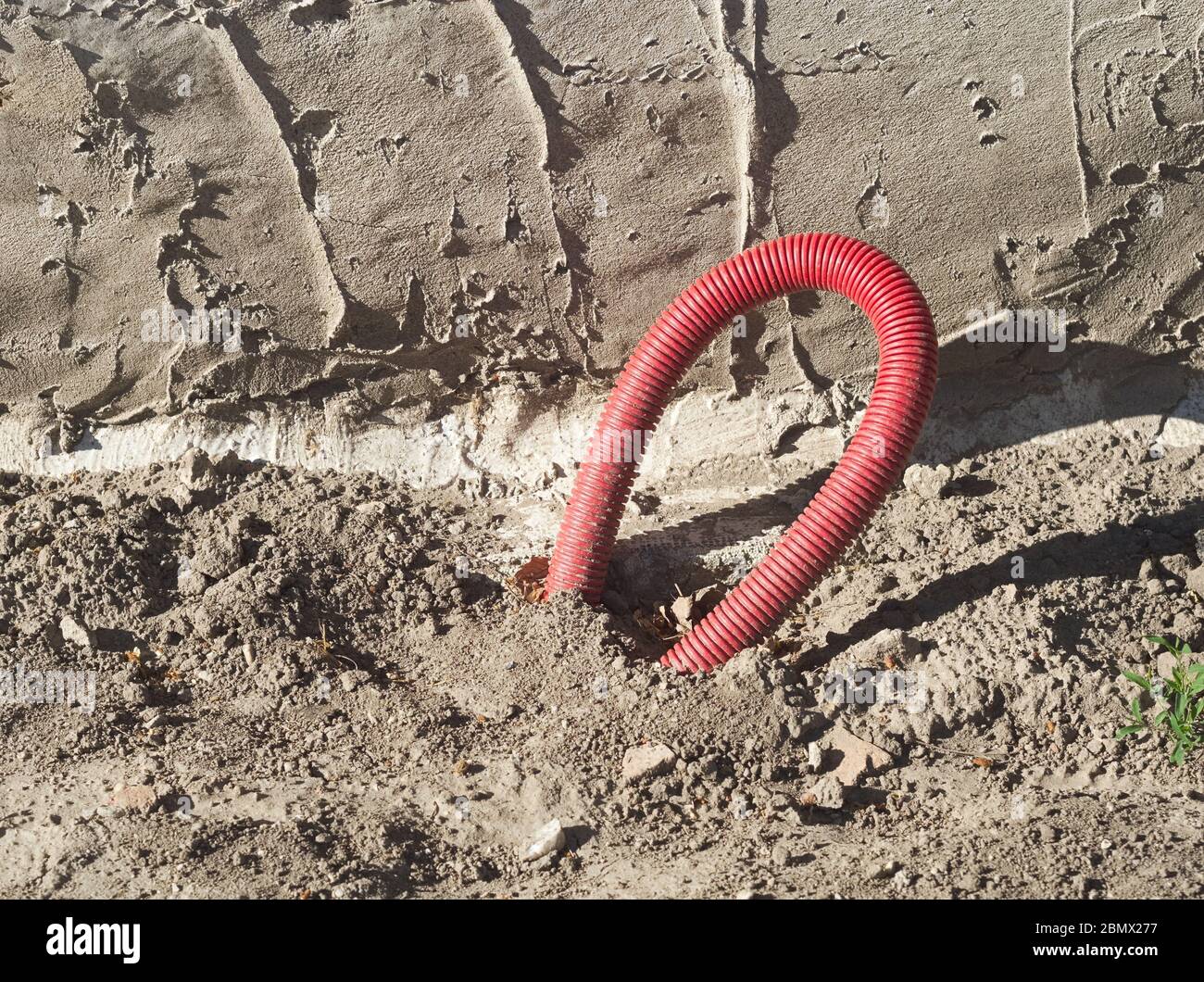 Cable eléctrico enterrado en la cubierta de plástico rojo del tubo Foto de stock
