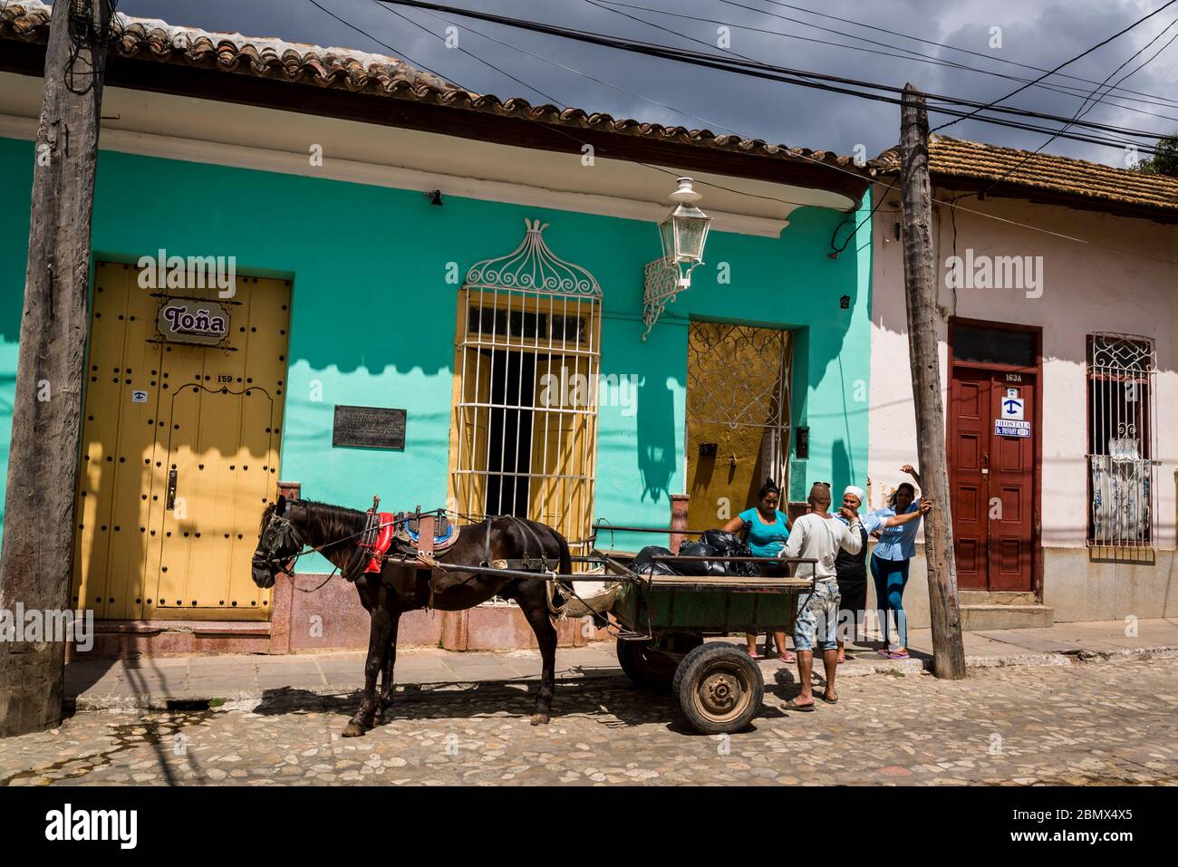 Caballo y carro recogiendo basura en una típica calle adoquinada con coloridas casas en el centro de la ciudad de la época colonial, Trinidad, Cuba Foto de stock