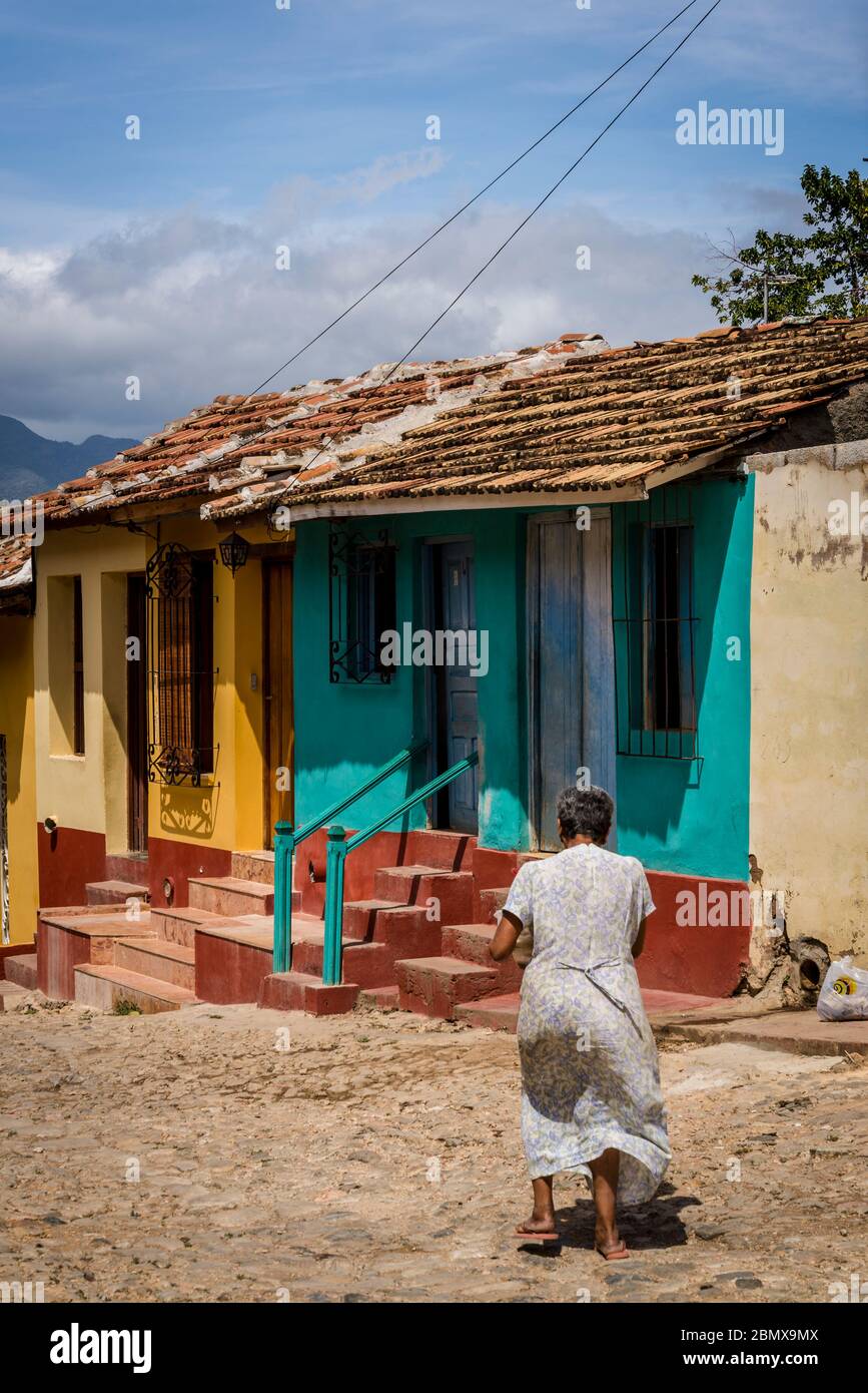 Mujer caminando en una típica calle adoquinada con coloridas casas en el antiguo centro colonial de la ciudad, Trinidad, Cuba Foto de stock