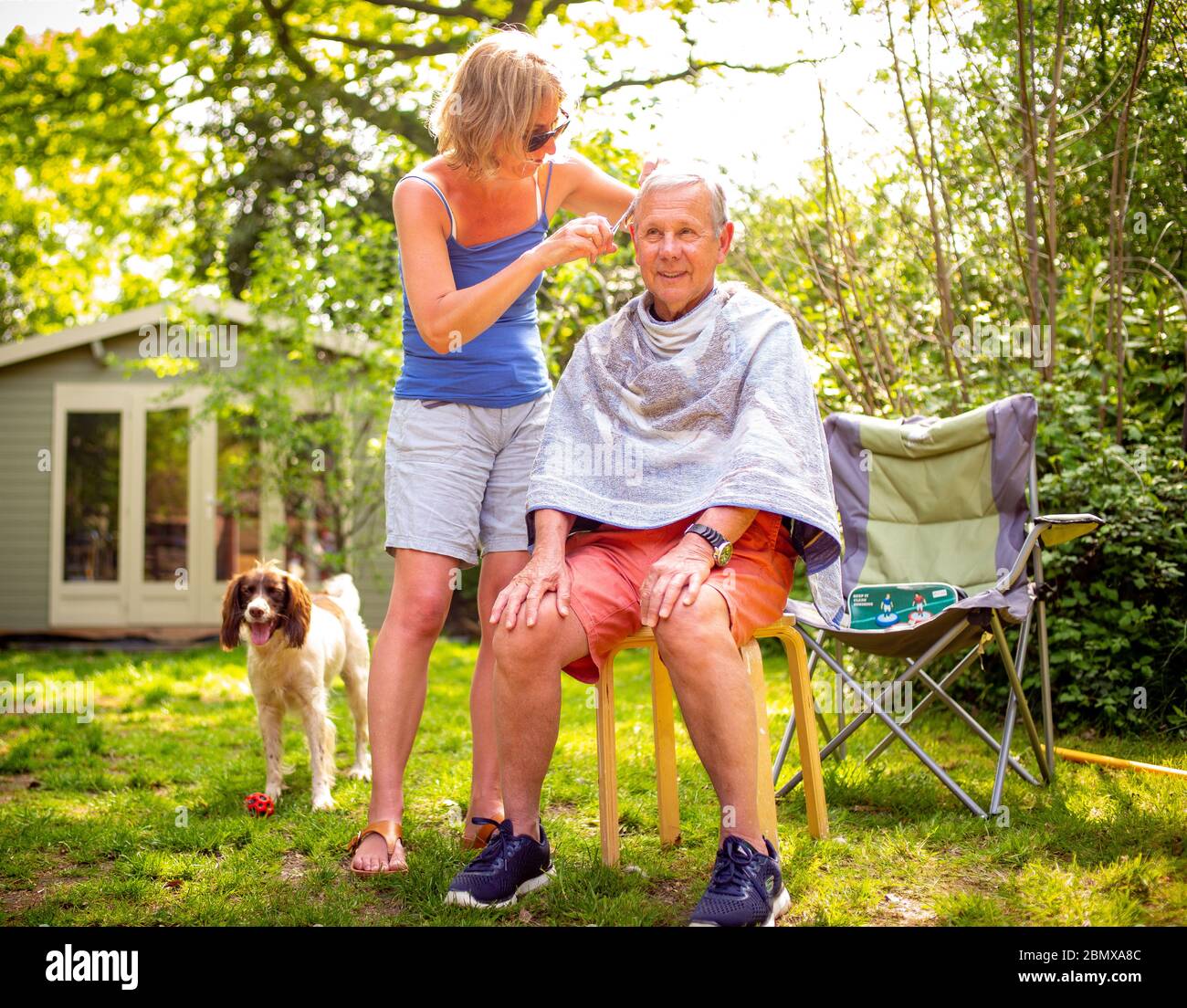 Aislar a su suegro le da un corte de pelo a su suegro durante el encierro en el jardín durante la pandemia del coronavirus. Foto de stock