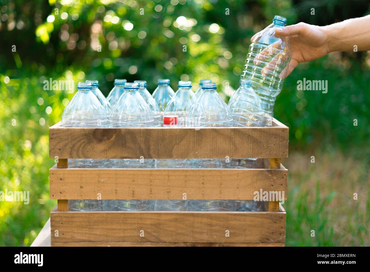 Reutilización de botellas de plástico concepto de reciclaje. Mano del  hombre dejando una botella de plástico en una caja de madera reciclada con  botellas de agua de plástico sin tapón con Fotografía