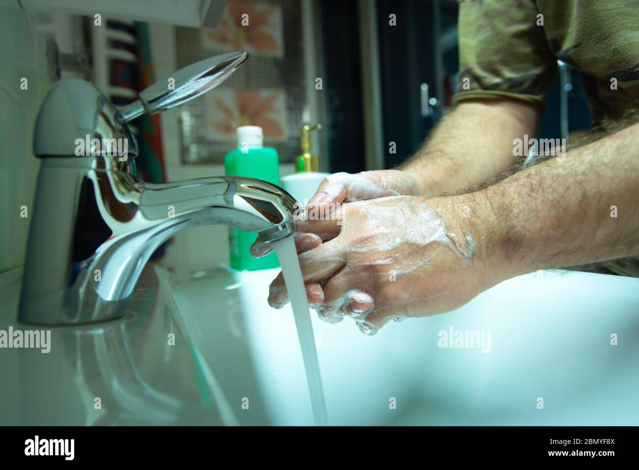 El hombre se lava las manos con jabón, vertiendo agua del grifo Foto de stock