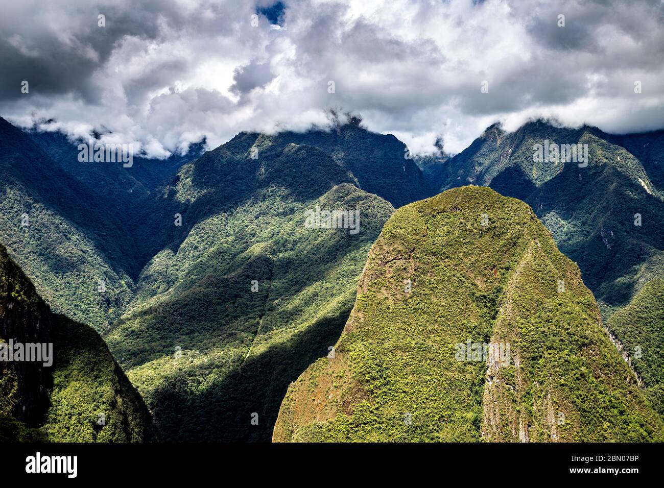 Nubes ominosas y exuberantes montañas verdes que rodean la antigua ciudad inca de Machu Picchu, Valle Sagrado, Perú Foto de stock