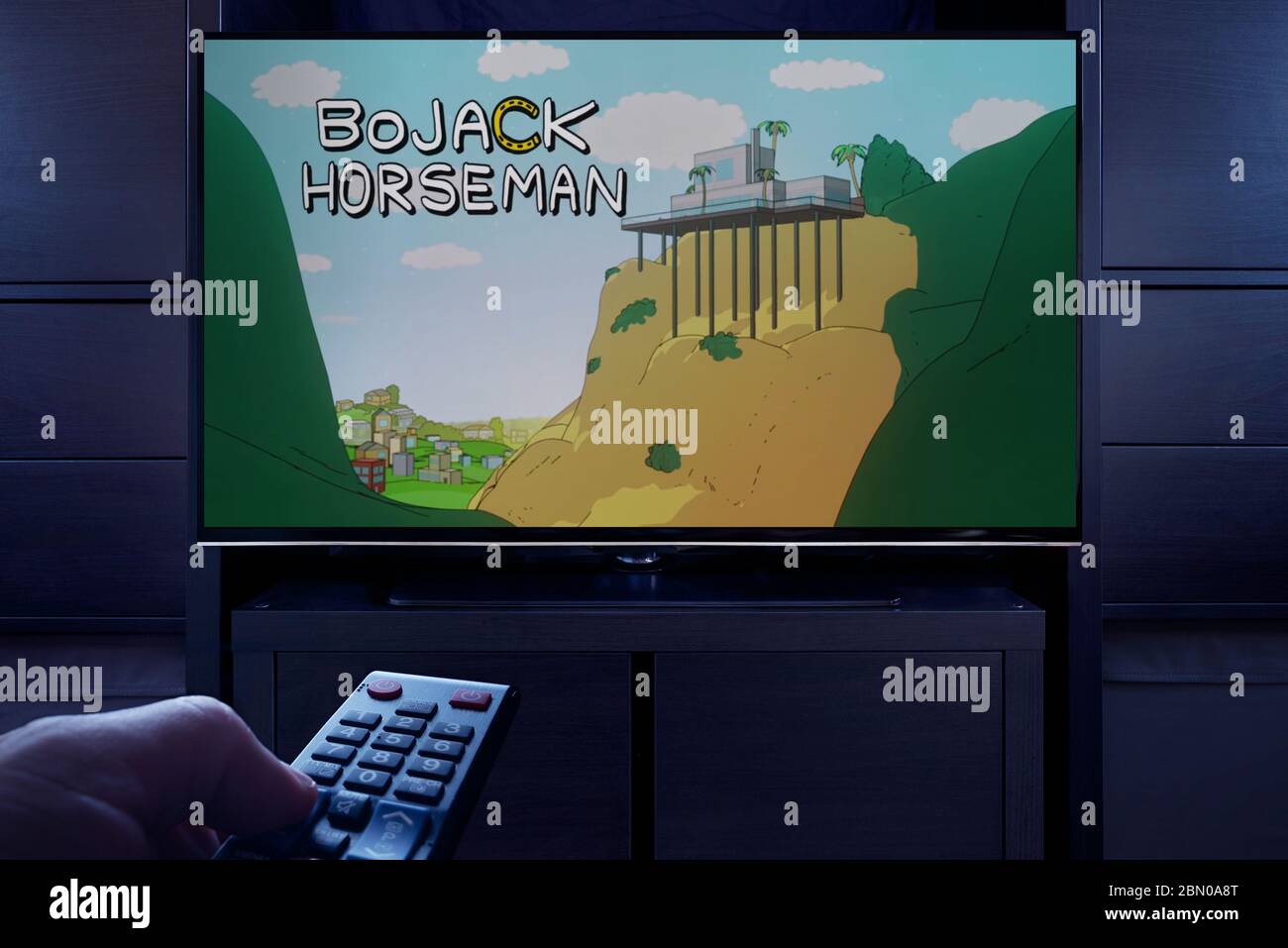 Un hombre apunta un mando a distancia de la televisión al televisor que muestra la pantalla principal del título de Bjack Horseman (sólo para uso editorial). Foto de stock