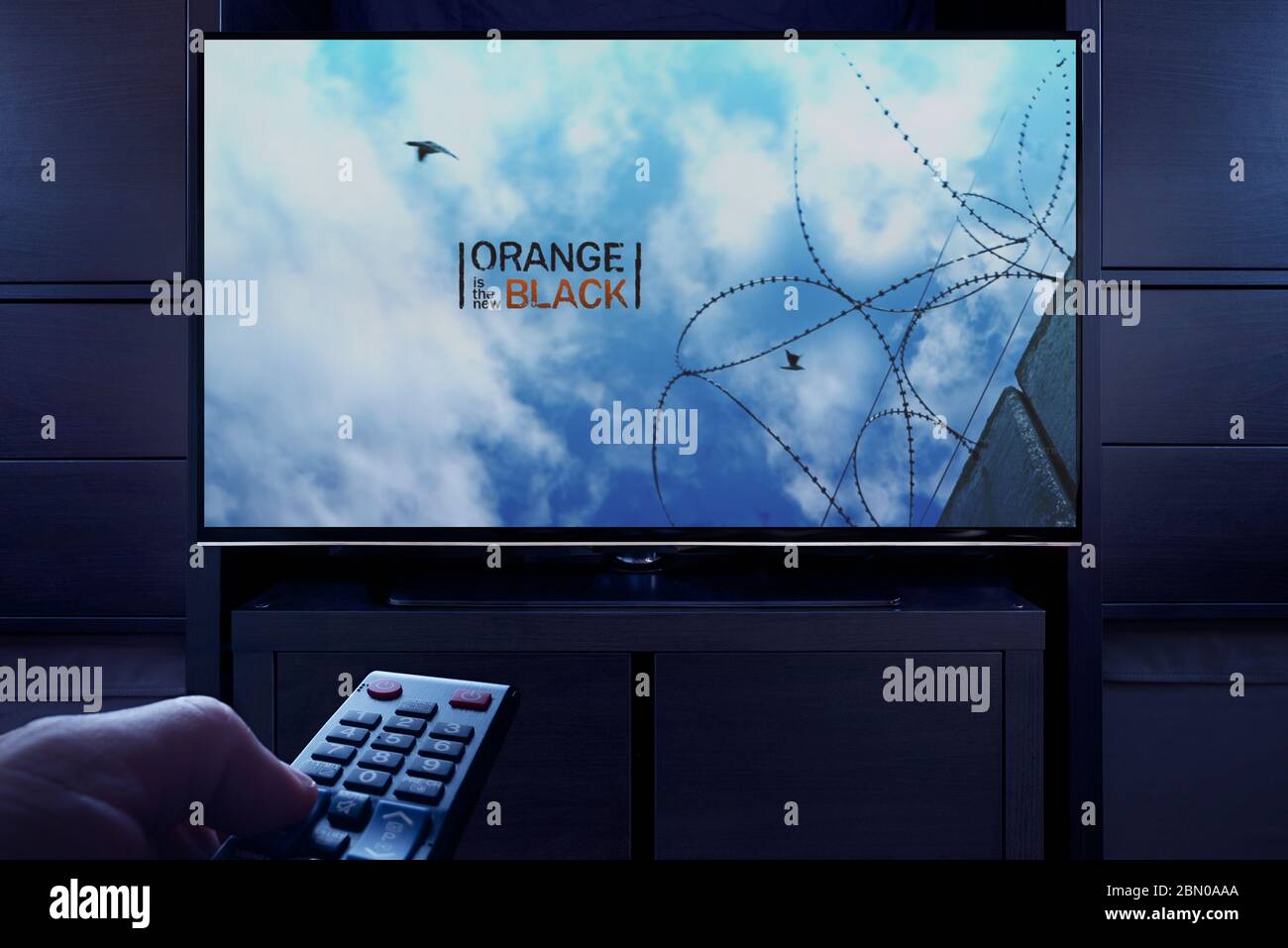 Un hombre apunta un mando a distancia de la televisión al televisor que muestra la pantalla principal de título de Orange es el New Black (sólo para uso editorial). Foto de stock
