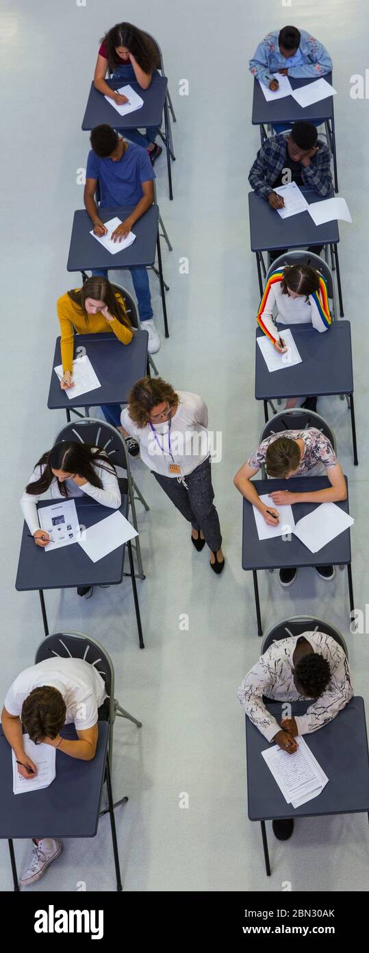 Maestro de secundaria que supervisa a los estudiantes que toman el examen en los escritorios Foto de stock