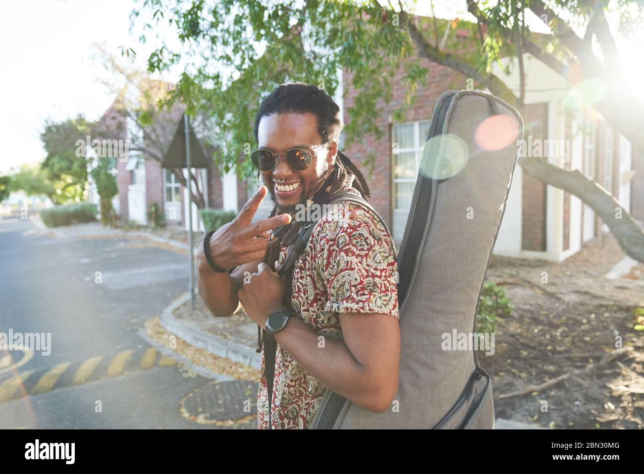 Retrato músico masculino feliz con caja de guitarra signo de paz gesturing Foto de stock