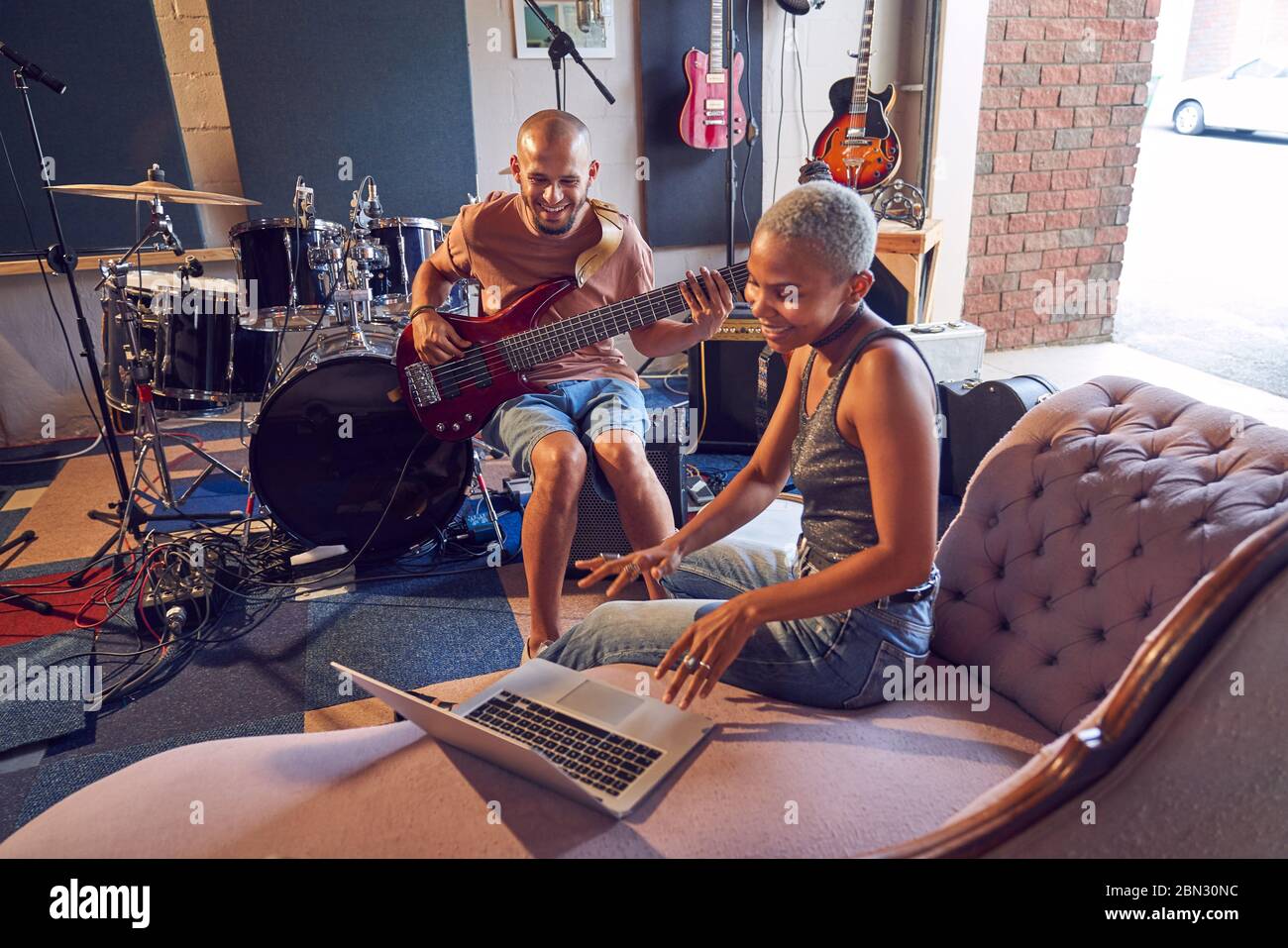 Músicos sonriendo con portátil y guitarra en estudio de grabación Foto de stock