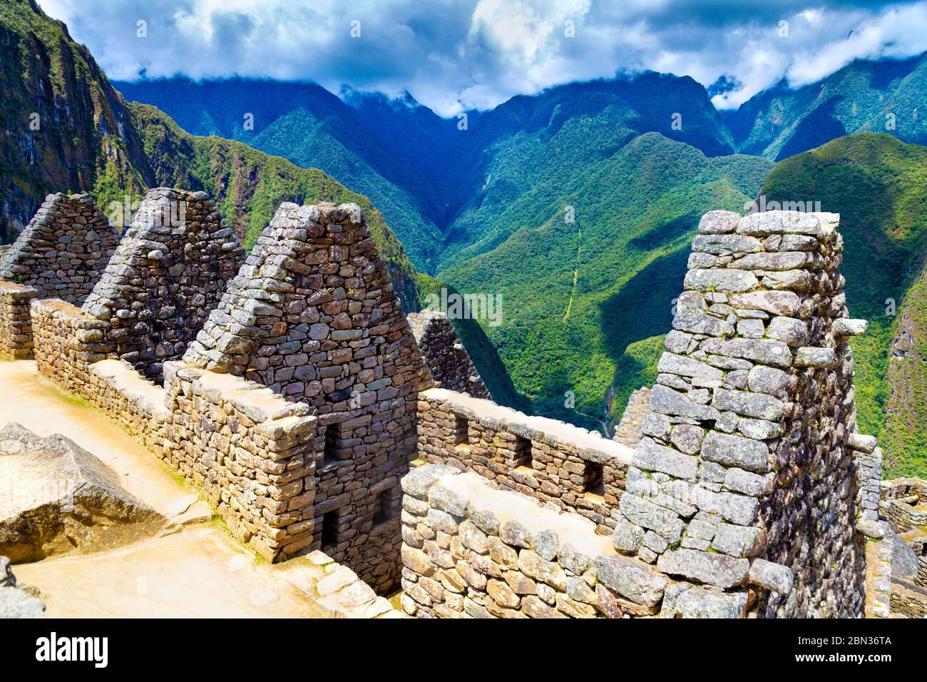 Ruinas de piedra de la antigua ciudad inca de Machu Picchu con espectaculares montañas y nubes en el fondo, Valle Sagrado, Perú Foto de stock