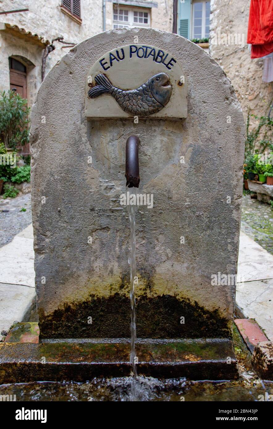 Una antigua fuente, llamada 'EAU POTABLE' (agua potable), con una imagen de un pez, distribuye agua en la ciudad de Saint-Paul-de-Vence, Francia Foto de stock