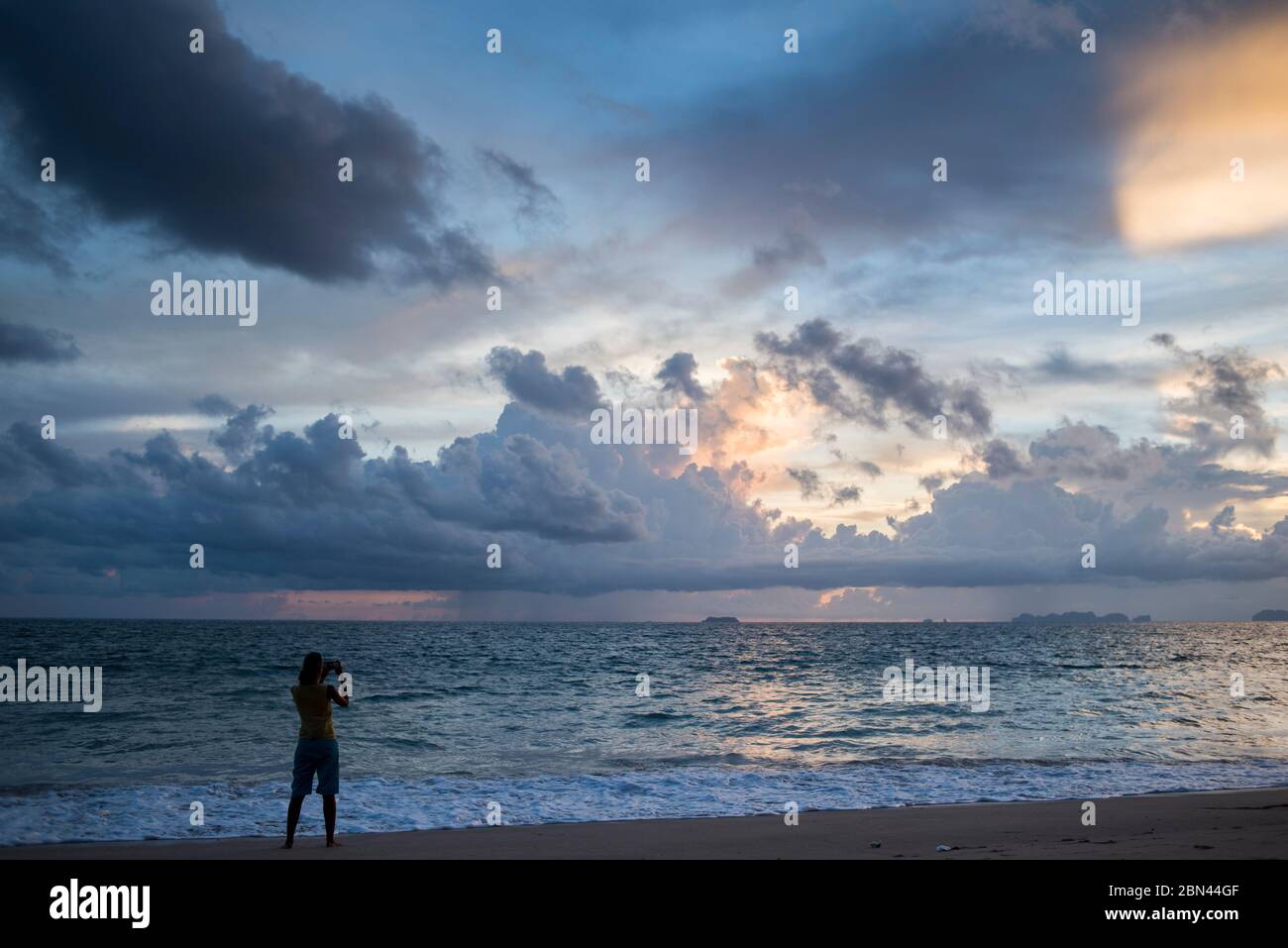 Una viajera que toma fotos al atardecer en una playa de la isla Koh Lanta, Tailandia. Foto de stock