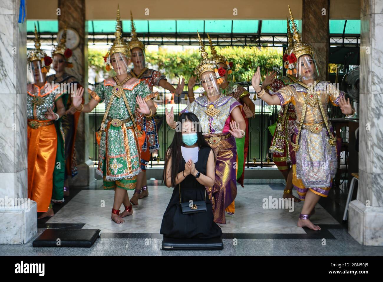 Bangkok, Tailandia. 5 de mayo de 2020. Bailarines tradicionales en el santuario de Erawan, un popular lugar turístico se realizan mientras que lleva protectores de cara junto a una mujer que ofrece oraciones, usando una máscara facial como precaución después de la facilidad gubernamental de algunas restricciones coronavirus durante el cierre. Crédito: Amphol Thongmueangluang/SOPA Imágenes/ZUMA Wire/Alamy Live News Foto de stock