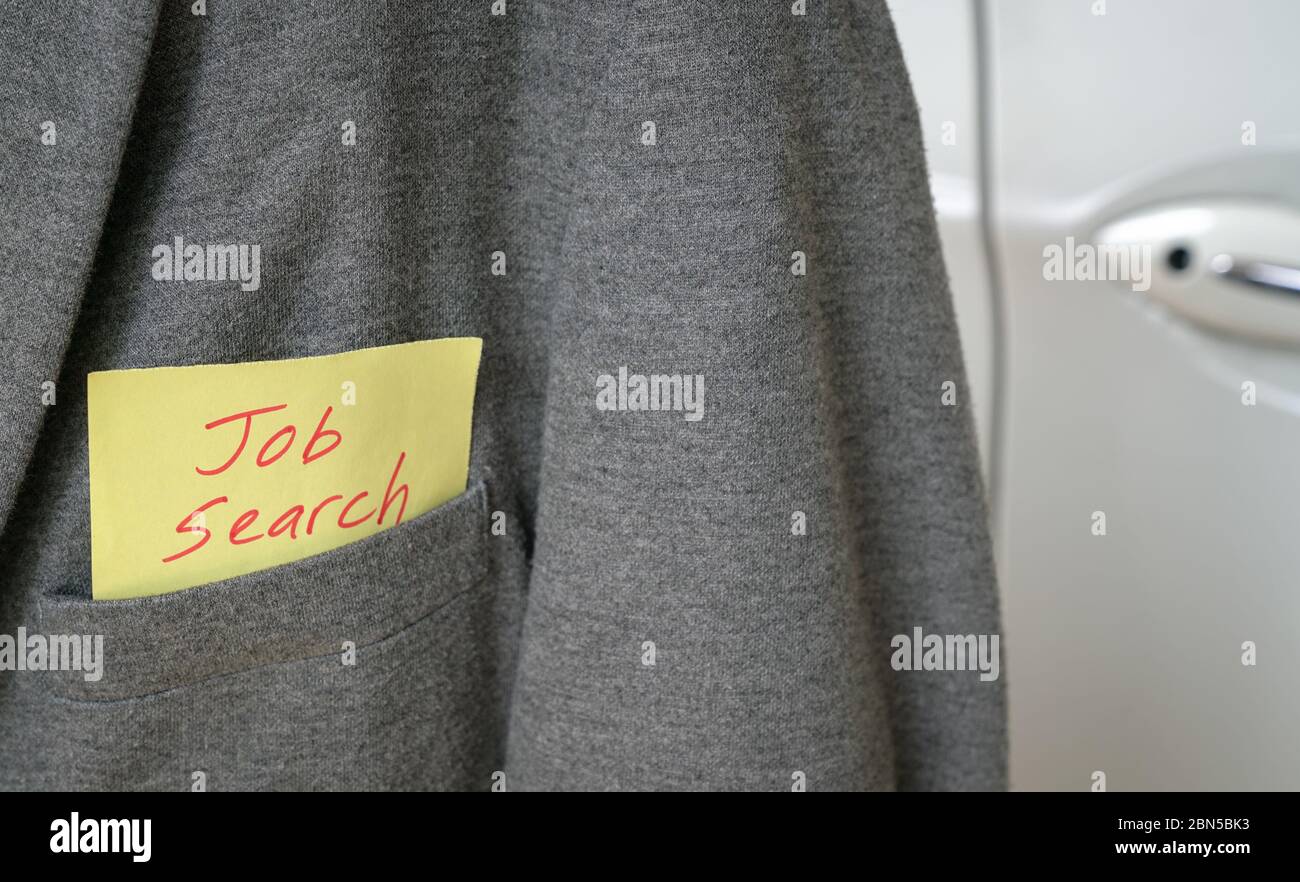 Búsqueda de trabajo, palabras en rojo en un papel amarillo pegadas fuera del bolsillo de una chaqueta gris. Coche blanco al fondo. Espacio de copia. Foto de stock