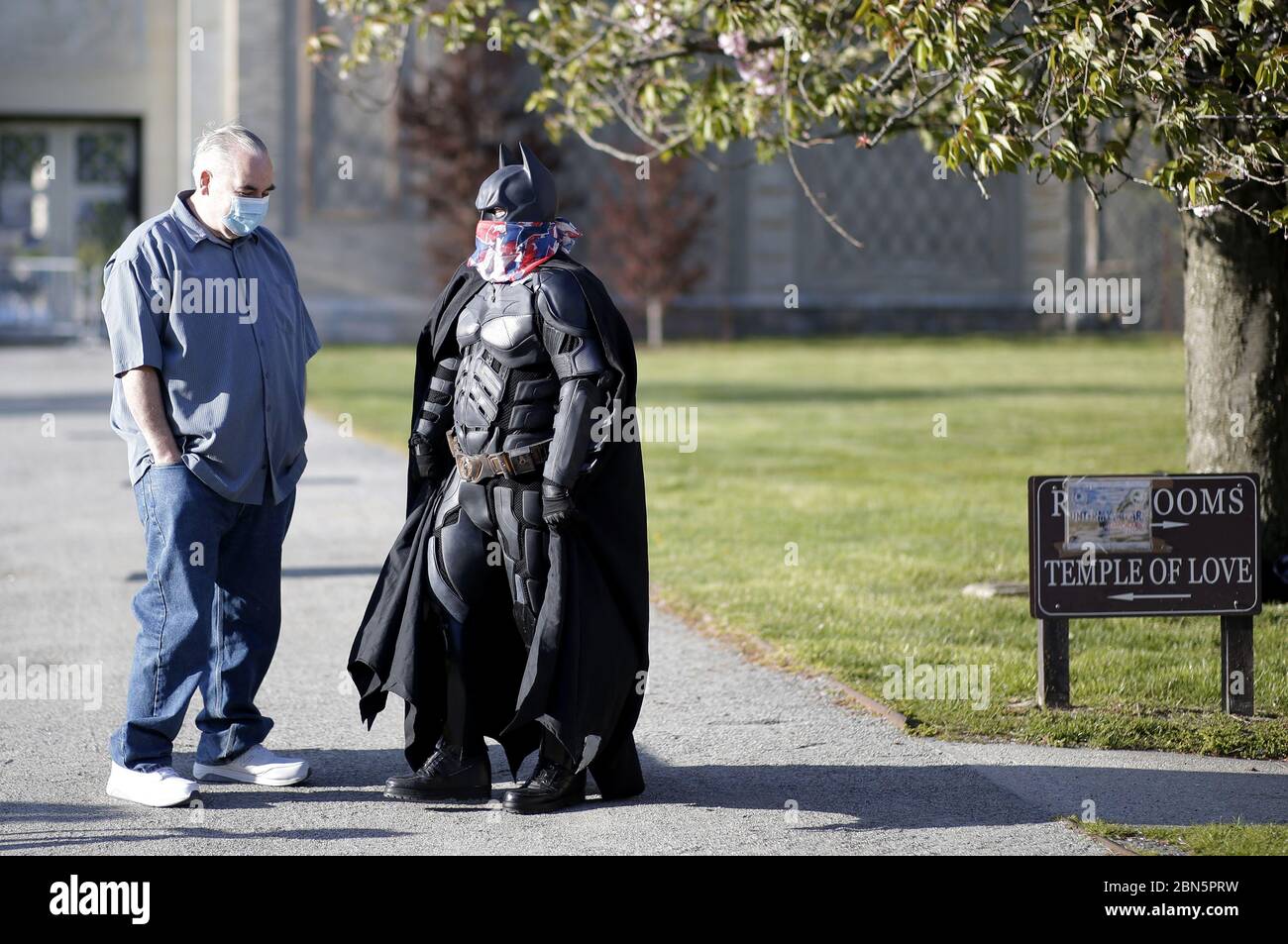 Un hombre vestido como superhéroe Batman lleva una máscara protectora  mientras habla con un hombre en telas sencillas mientras enfermeras,  funcionarios electos y miembros de la comunidad se reúnen para conmemorar el