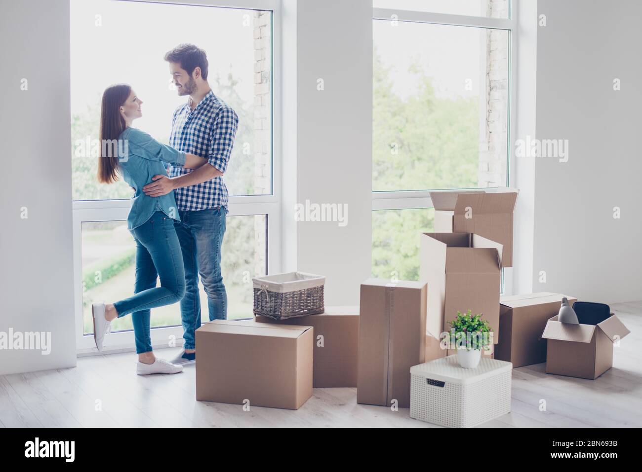 Feliz pareja joven se trasladó a un nuevo lugar para empezar a vivir juntos, están abrazando, alrededor de muchas cajas de cartón con sus cosas. La habitación es muy luminosa Fotografía de Feliz pareja joven se trasladó a un nuevo lugar para empezar a vivir juntos, están abrazando, alrededor de muchas cajas de cartón con sus cosas. La habitación es muy luminosa Fotografía de