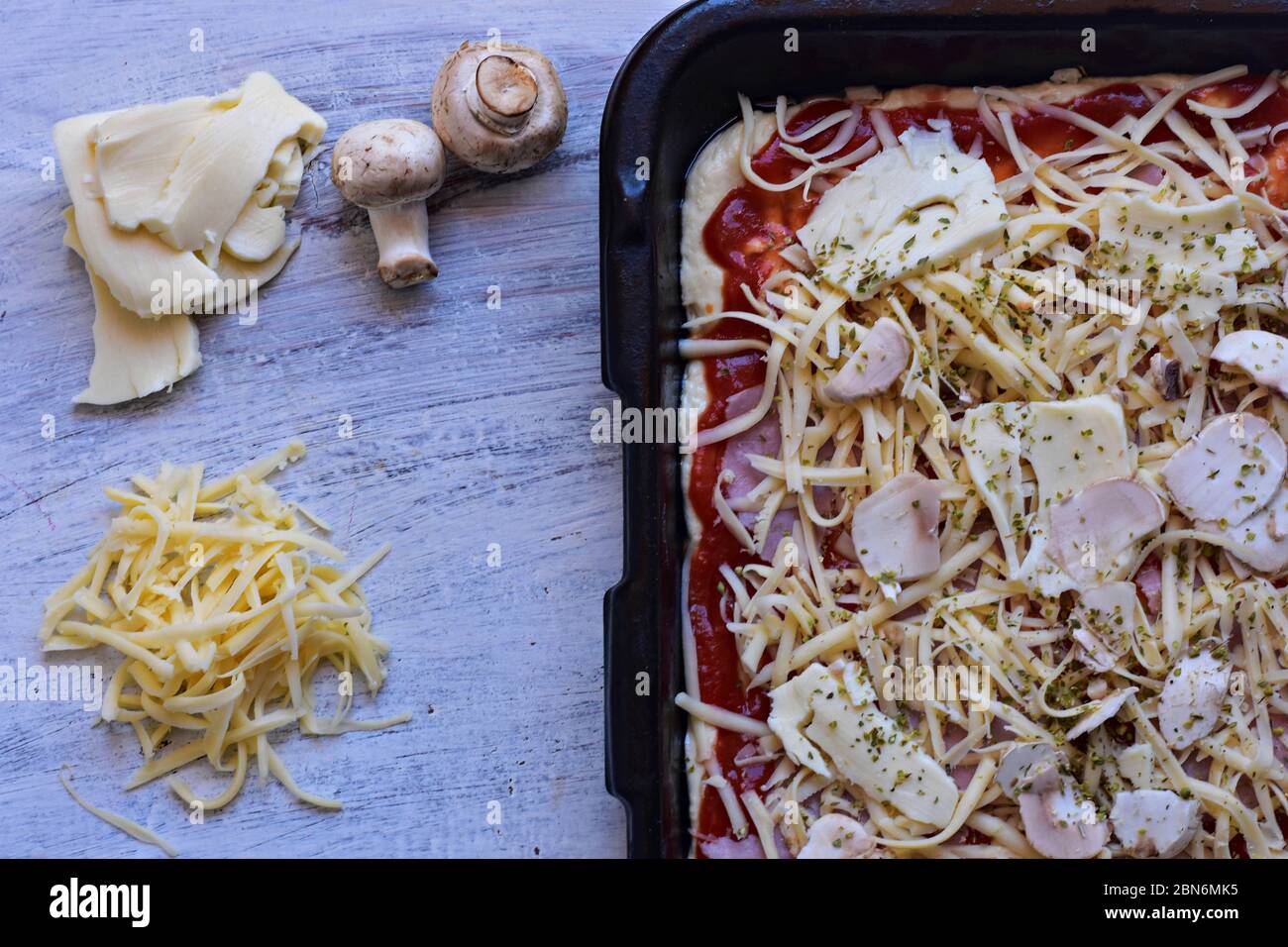 Masa para pizza con salsa de tomate, queso rallado, champiñones y mozzarella en madera cubiertos de fondo// FONDO DE ALIMENTOS Foto de stock