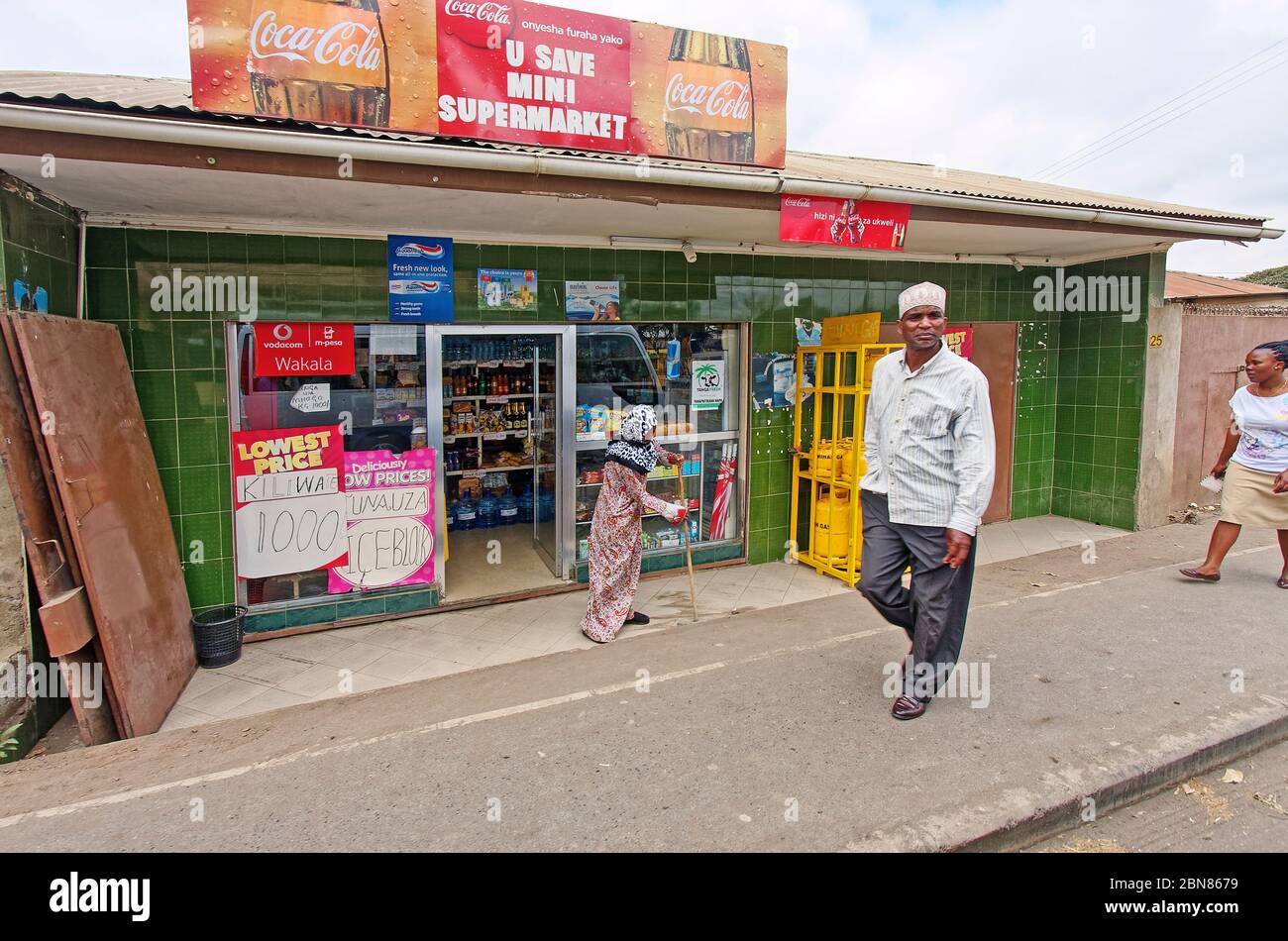 Escena Callejera Mini Supermercado Mujer Barriendo Gente Caminando Movimiento Acera Senales Negocios Venta De Alimentos Africa Arusha Tanzania Fotografia De Stock Alamy