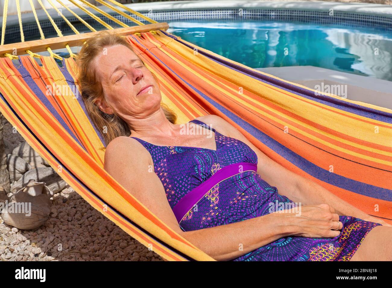 Mujer holandesa de mediana edad, tumbada en una colorida hamaca cerca de la piscina Foto de stock
