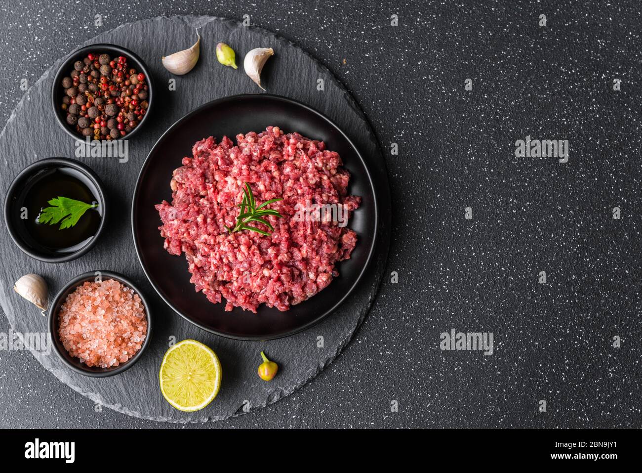 Carne picada fresca molida de carne en un plato negro sobre fondo de piedra. Foto de stock