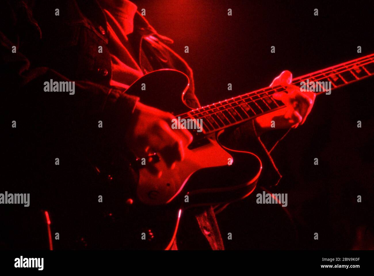 Primer plano de guitarrista tocando guitarra eléctrica en vivo bajo iluminación roja. Londres 1991, banda de rock desconocida. Foto de stock