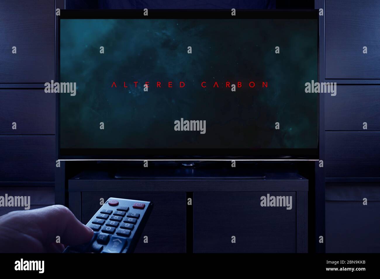 Un hombre apunta un mando a distancia de la televisión al televisor que muestra la pantalla de título principal de Carbon alterado (sólo para uso editorial). Foto de stock