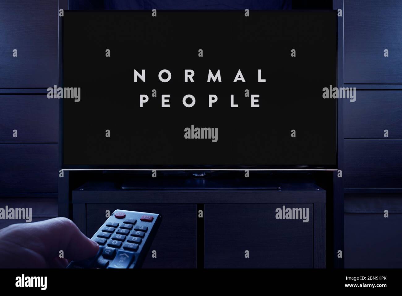 Un hombre apunta un mando a distancia de la televisión al televisor que muestra la pantalla de título principal de personas normales (sólo para uso editorial). Foto de stock