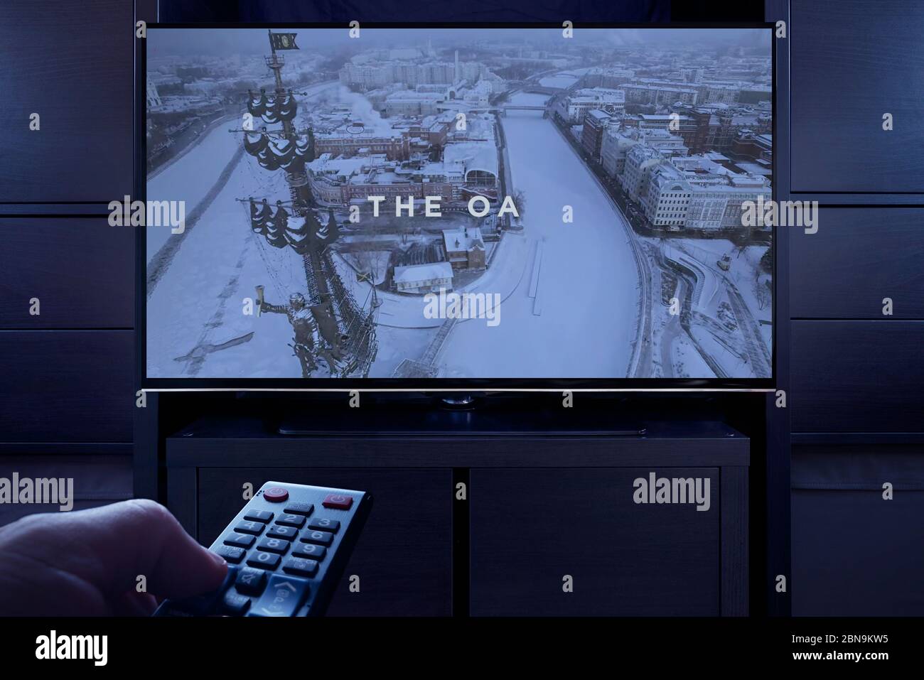 Un hombre apunta un mando a distancia de la televisión al televisor que muestra la pantalla principal del título de OA (sólo para uso editorial). Foto de stock
