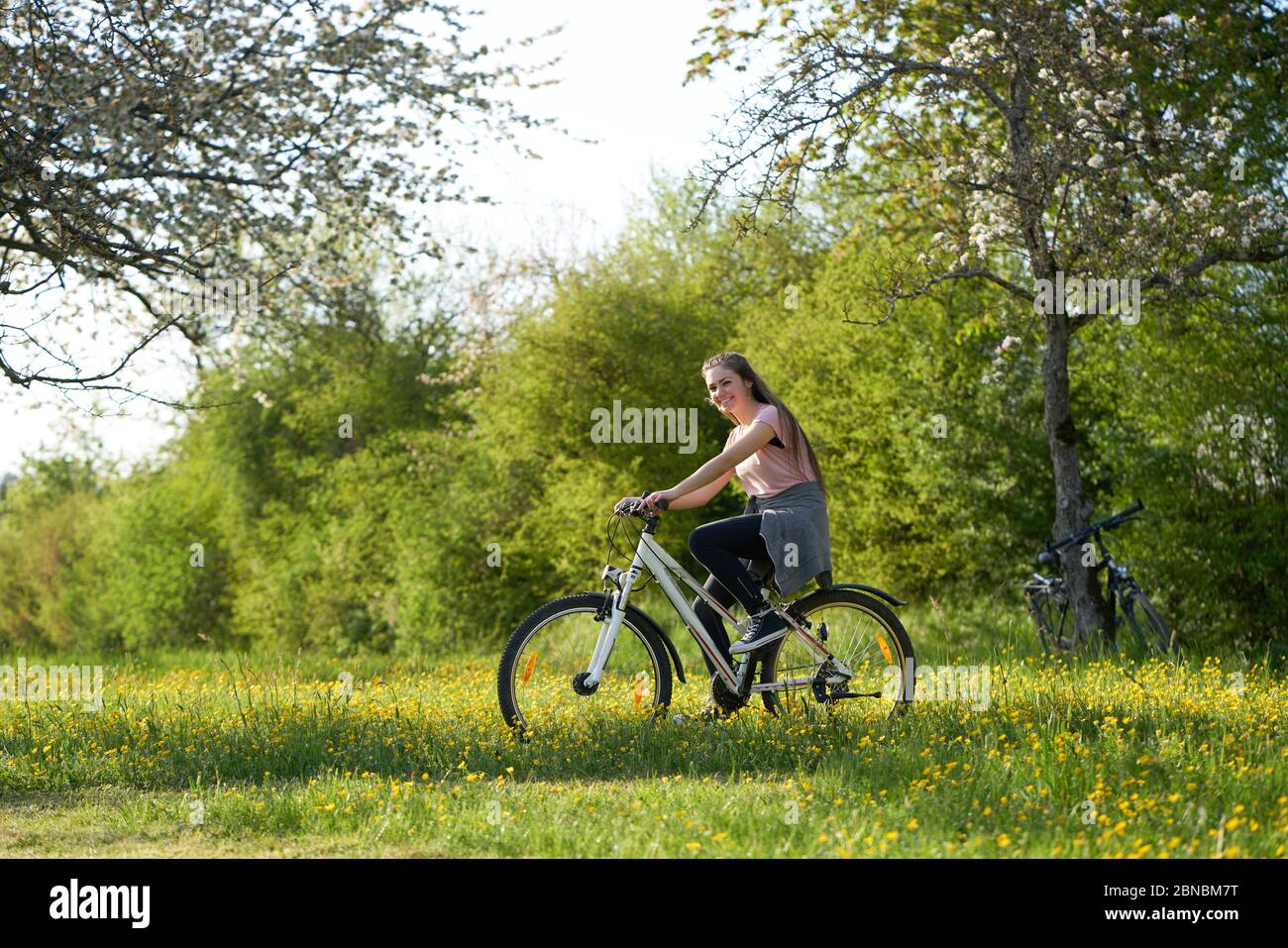 Joven sonriente en bicicleta en un prado con flores amarillas, en el fondo  arbustos y bicicletas apoyado en un manzano Fotografía de stock - Alamy