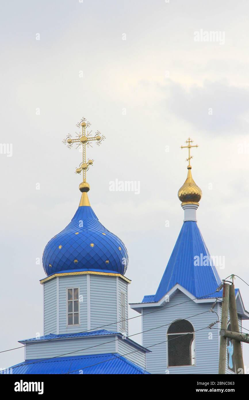 Iglesia cristiana ortodoxa con paredes blancas, cúpulas azules y cruces doradas en Rusia. Un edificio para ceremonias religiosas con un campanario contra un cielo nublado en el campo. Foto de stock