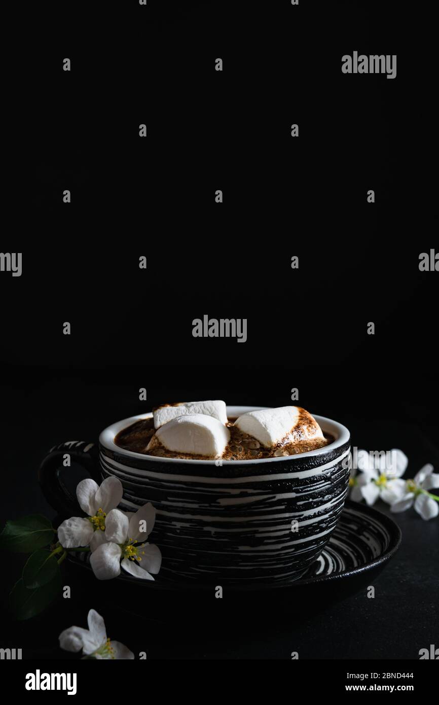 vida quieto, taza de café con malvaviscos y flores de primavera sobre un fondo negro, espacio vacío para el texto Foto de stock