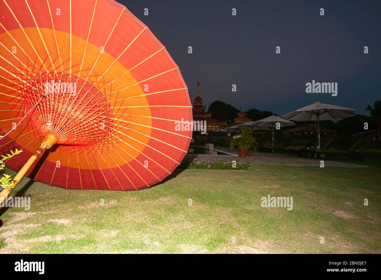 La luz ilumina el paraguas asiático tradicional rojo brillante y naranja en el suelo con fondo oscuro y el cielo detrás. Foto de stock