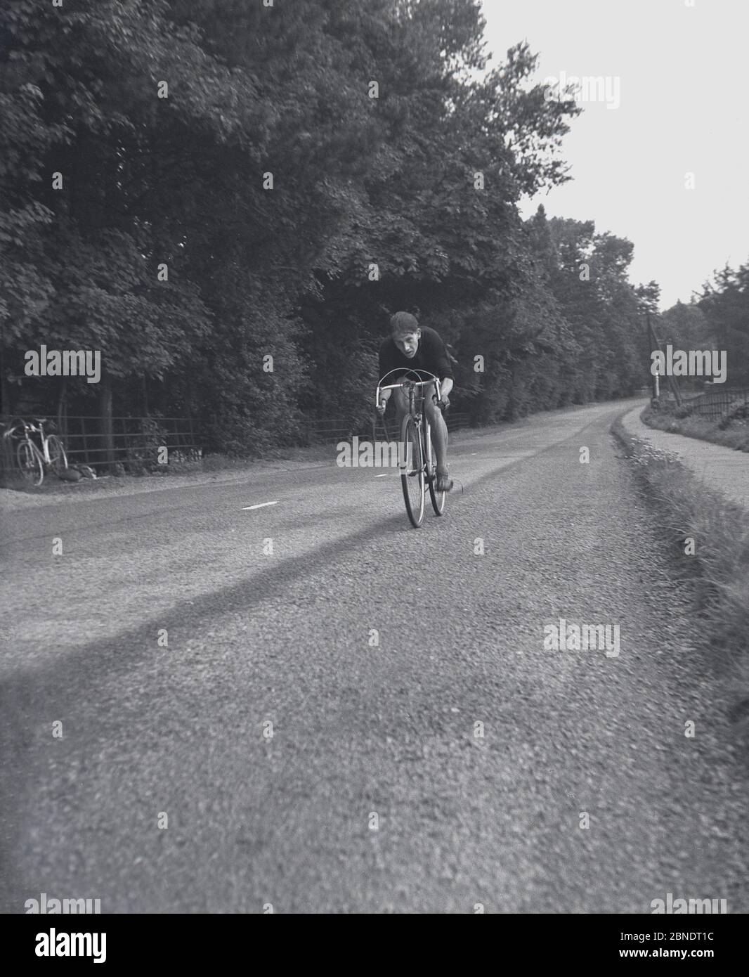 1950, histórico, un ciclista en una bicicleta de carreras a lo largo de una carretera rural vacía, posiblemente en un evento de prueba de tiempo, Inglaterra, Reino Unido. Foto de stock