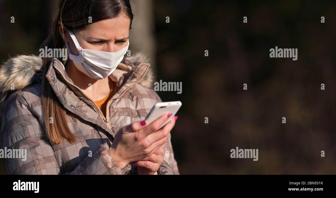 Mujer joven con chaqueta de abrigo, con máscara blanca de algodón virus, comprobando su teléfono móvil. Coronavirus concepto de prevención de Fotografía de stock - Alamy
