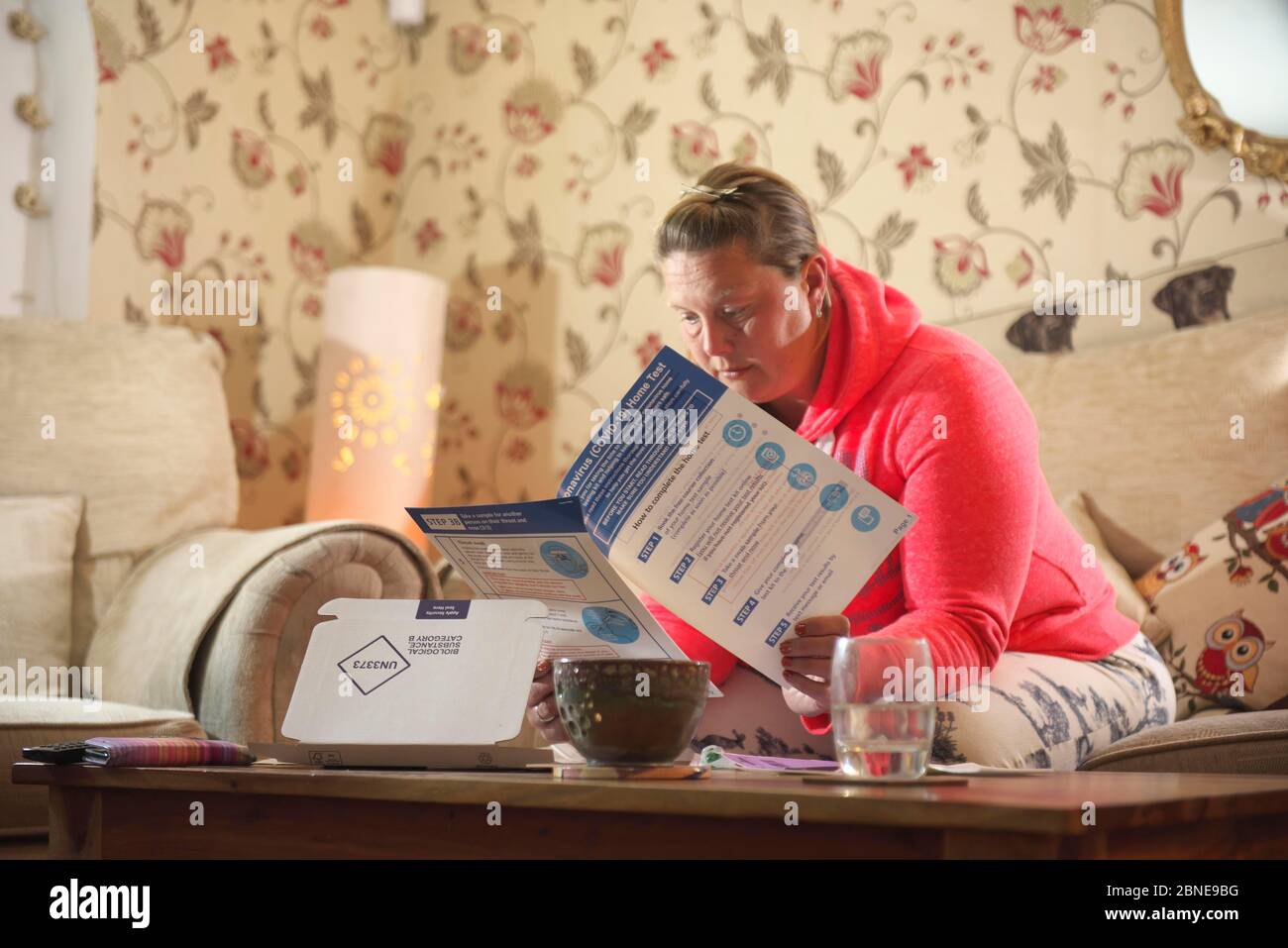 joven de mediana edad mirando mujer blanca se sienta en casa leyendo a través de Covid19 kit de pruebas en casa suministrado por el gobierno del Reino Unido Foto de stock