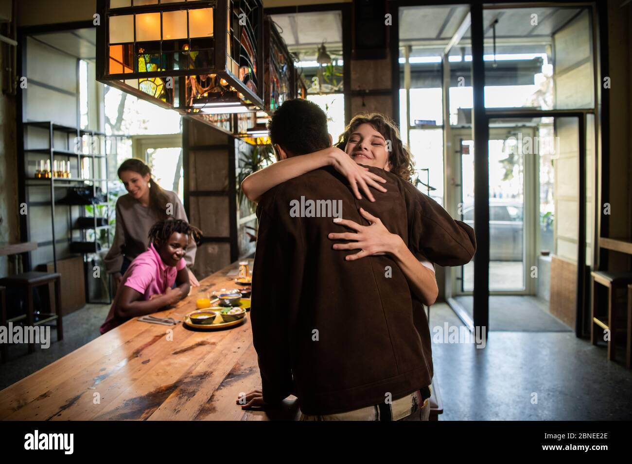 Una chica joven y bonita abrazando a un chico en un café para saludarlo, su Foto de stock