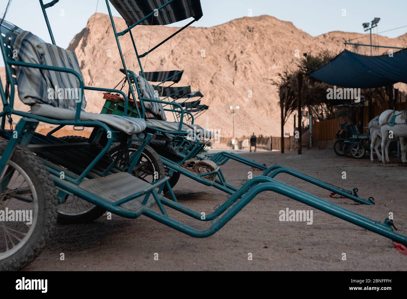 Carros de metal cerca de un establo y las tiendas en un desierto rodeado de montañas Foto de stock