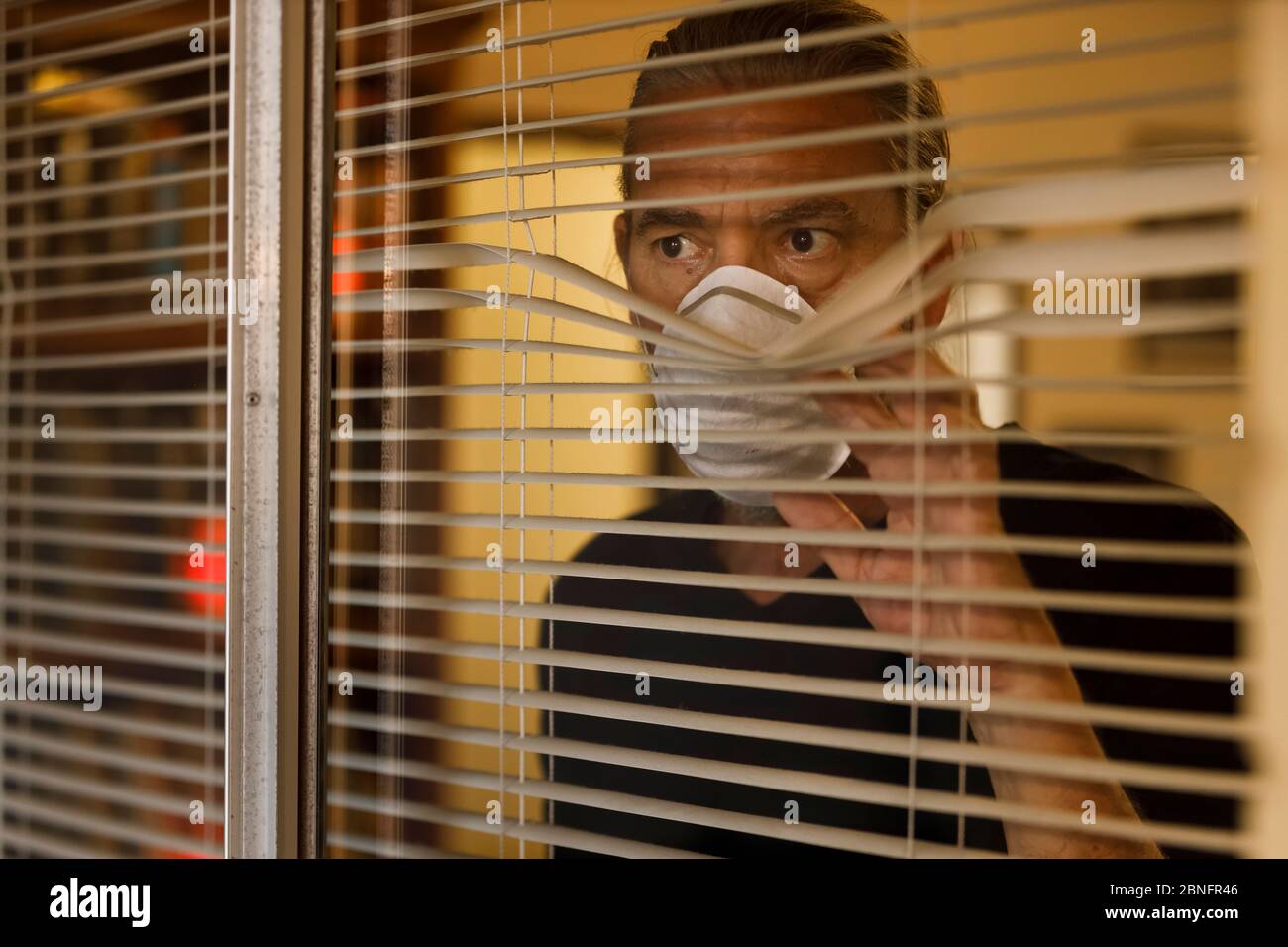coronavirus, hombre usando máscara médica en el aislamiento de uno mismo mirando fuera de las persianas de la ventana de la casa. El hombre preocupado toma las medidas de seguridad de cuarentena de Covid 19 Foto de stock