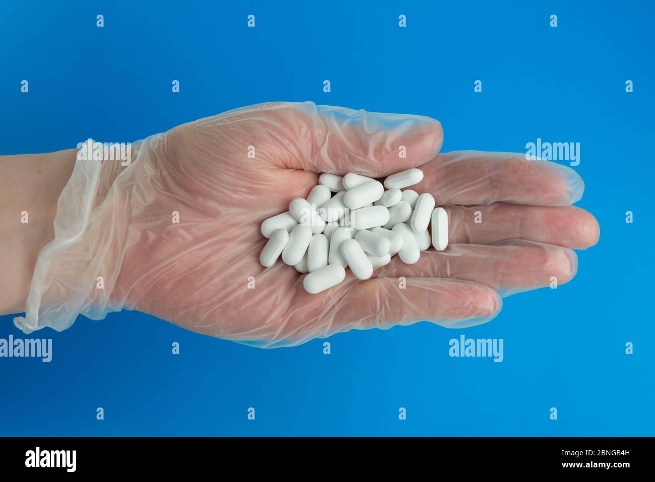 La mano del doctor en guante médico sostiene muchas píldoras blancas. Foto de stock
