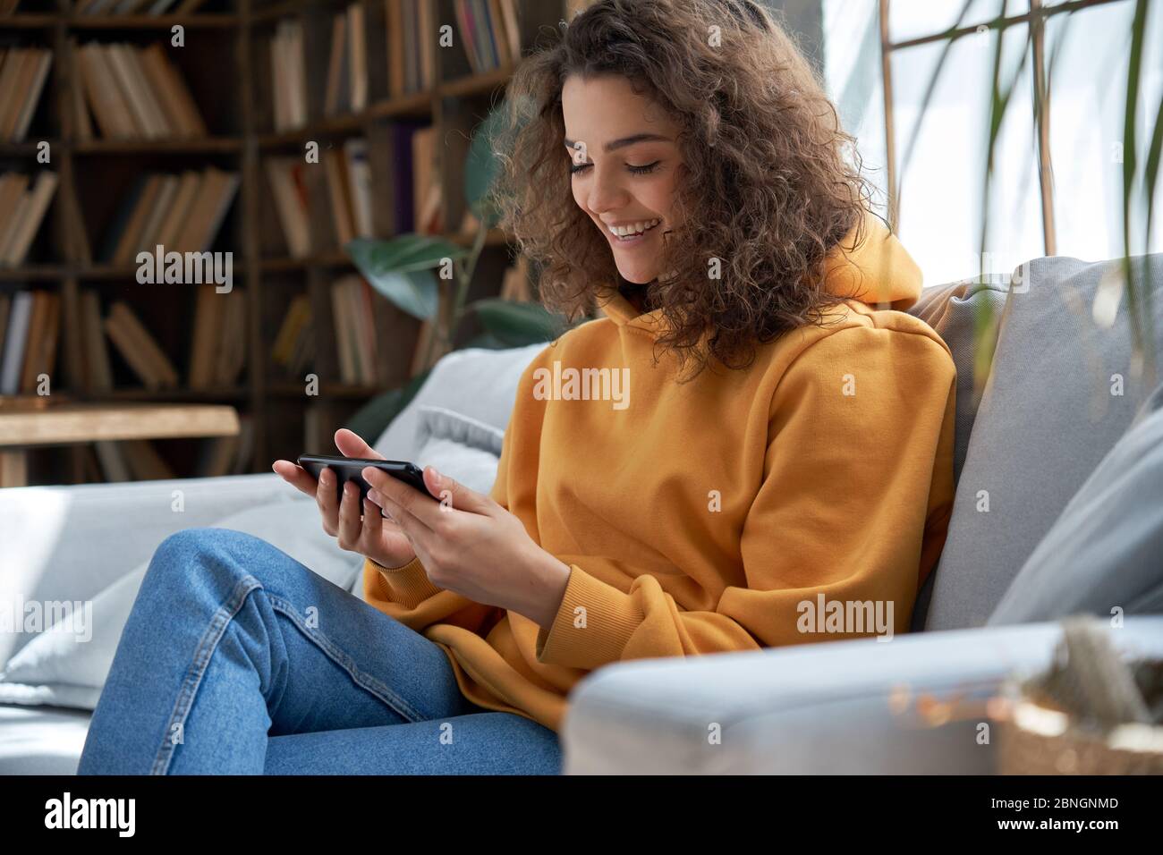 Feliz niña hispana en casa viendo video en las redes sociales en línea usando un teléfono inteligente. Foto de stock