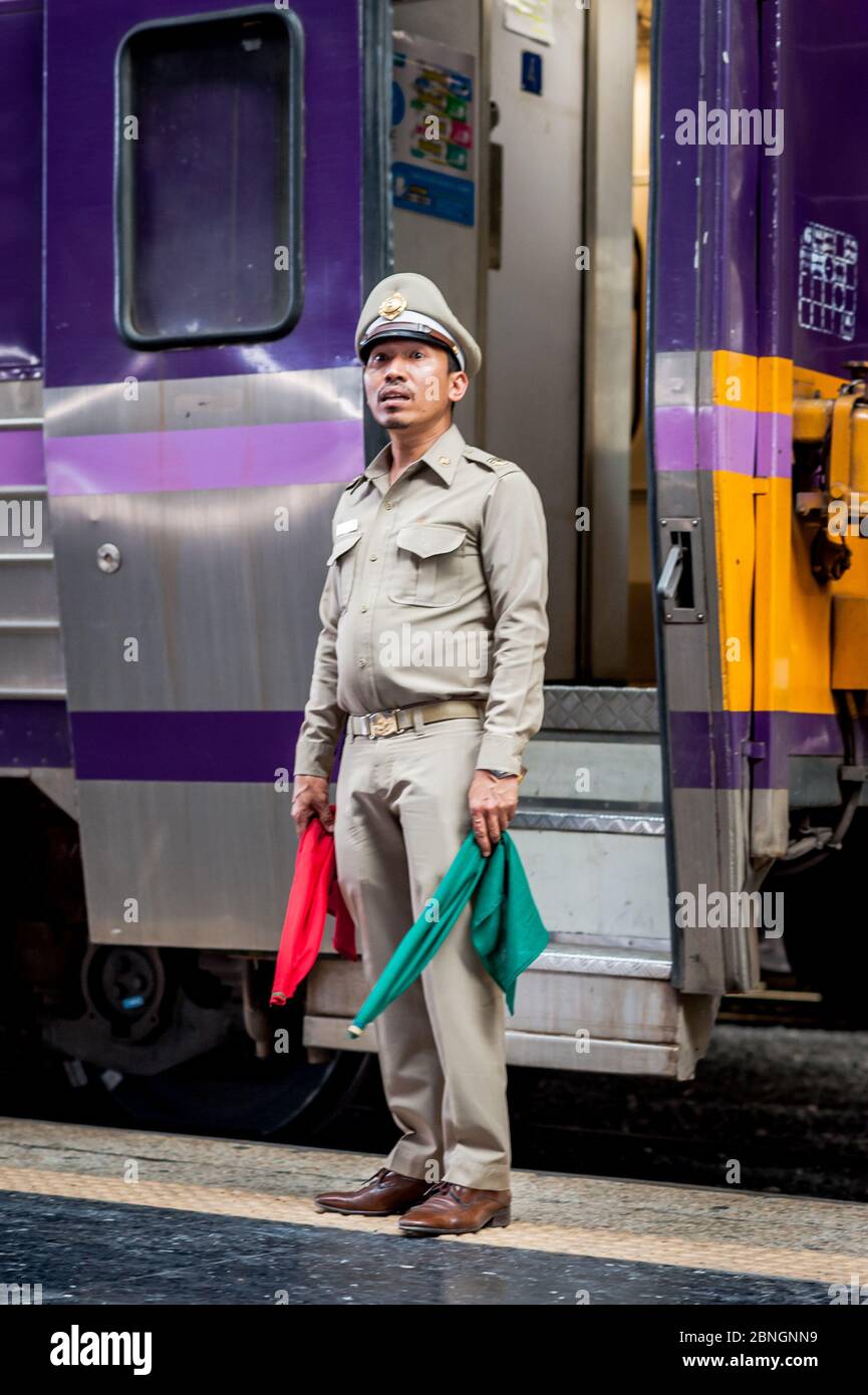 Un orgulloso guardia espera para dar a todos claro en una plataforma en la estación de tren de Hua Lamphong, Bangkok, Tailandia. Foto de stock