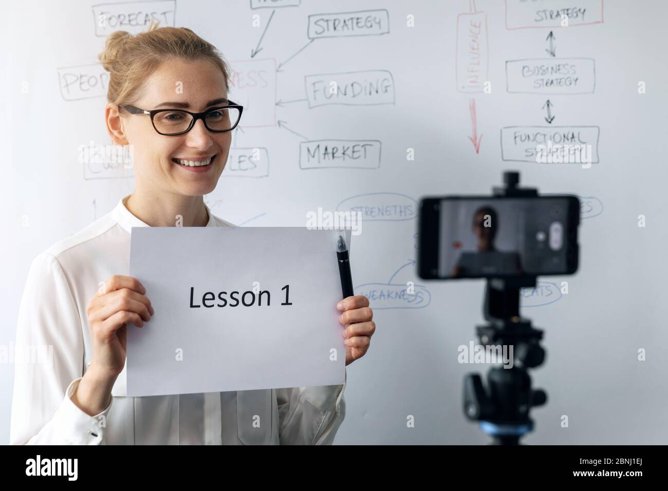 educación en línea, seminario web y el concepto de vlog empresarial - mujer enseñando y grabando vídeo con el teléfono en frente de la pizarra Foto de stock