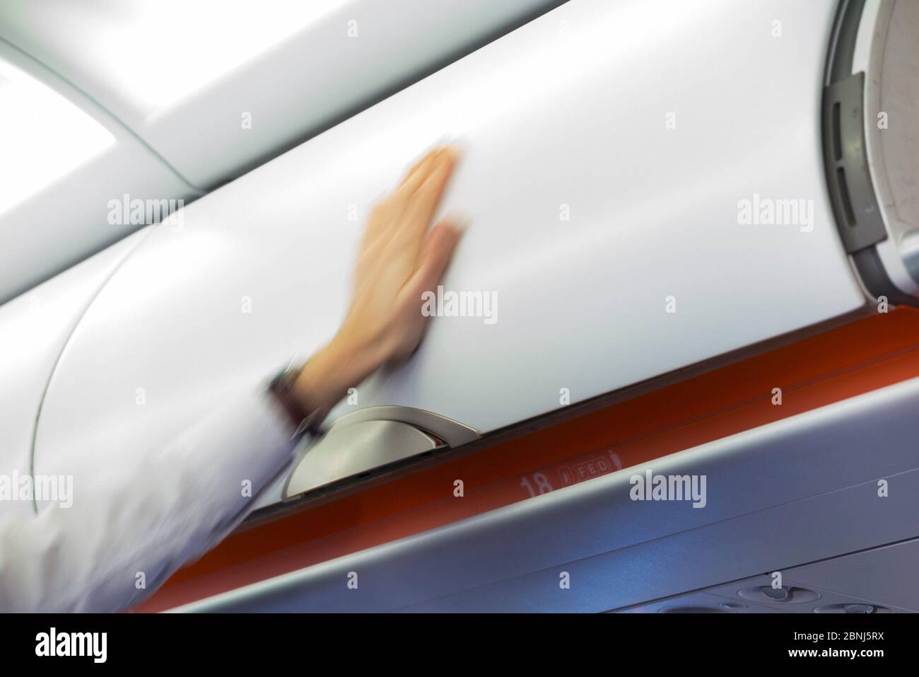 El miembro del asistente de vuelo de la tripulación de cabina cierra el avión aéreo sobre el depósito de equipaje / casilleros / compartimentos / puerta que contiene las bolsas de mano de los pasajeros. (115) Foto de stock