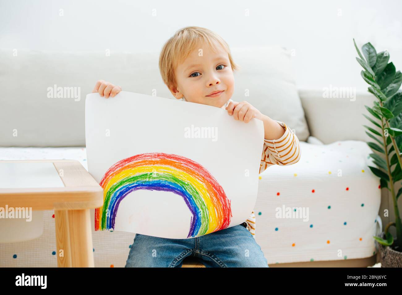 Lindo niño mostrando un arco iris que acaba de pintar en una hoja de papel Foto de stock