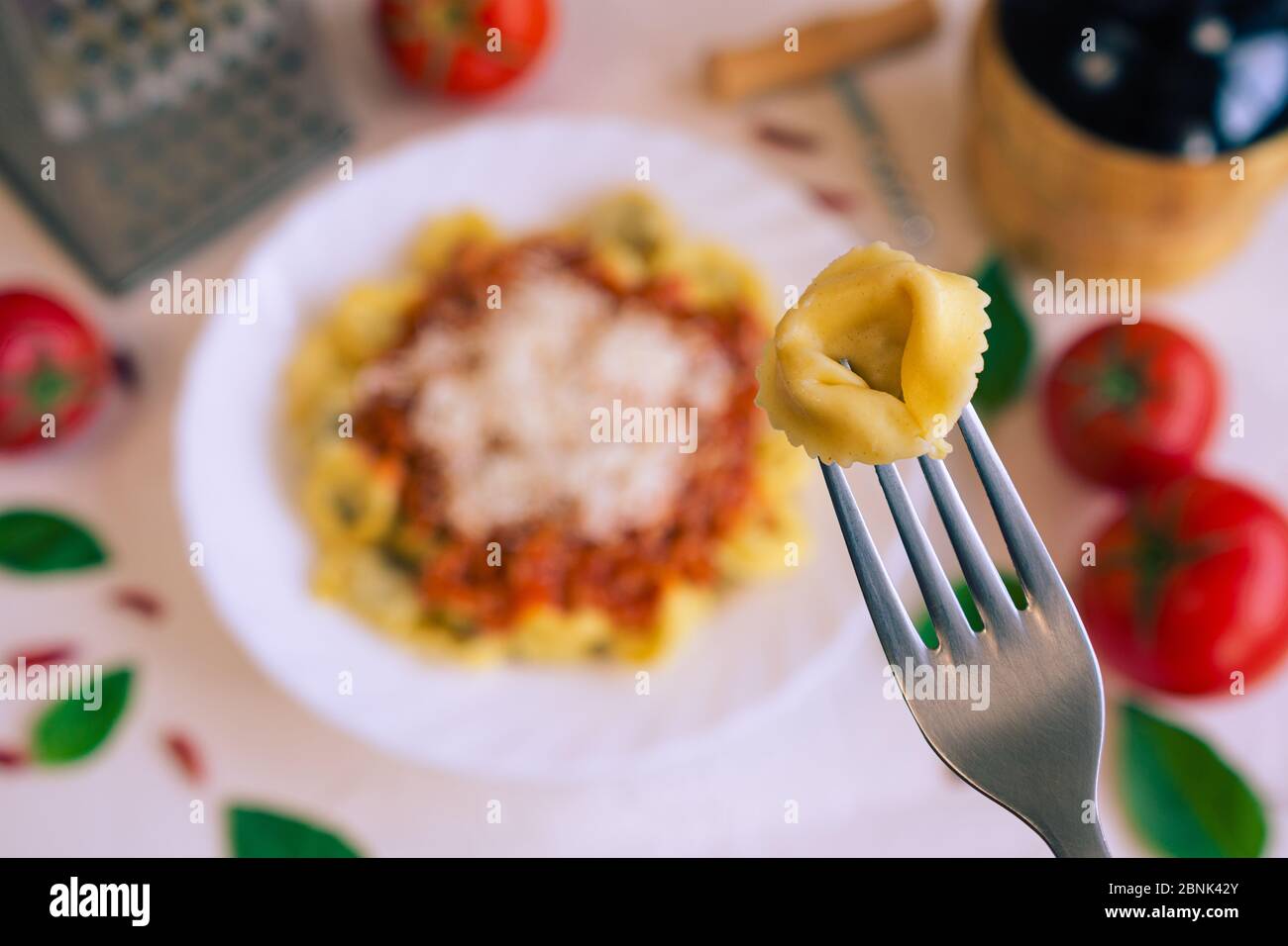 Un cappelletti en un tenedor y en el fondo una mesa con comida típica italiana Foto de stock