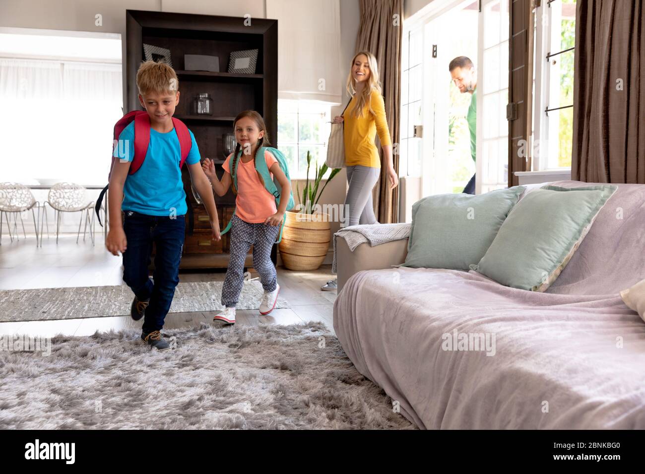 Familia caucásica con dos niños entrando en su casa regresando de la escuela Foto de stock