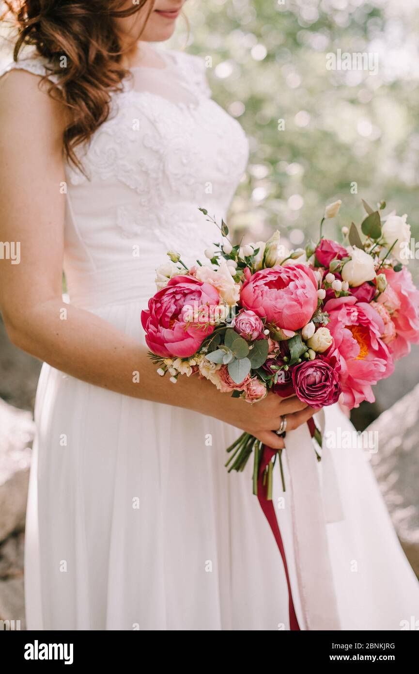 Ramo de novia primer plano, el ramo consiste en peonías rojas, rosas rojas  y blancas. La novia sostiene el ramo Fotografía de stock - Alamy