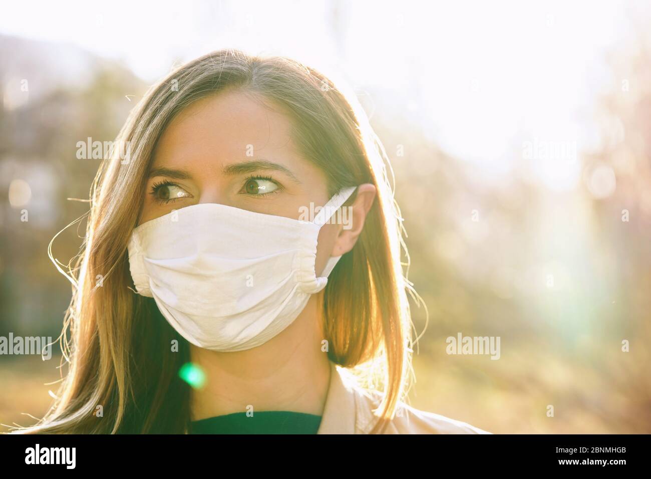 Mujer joven con piel blanca de algodón virus boca máscara nasal, buena luz de fondo sol bokeh en el fondo, primer plano retrato facial Foto de stock