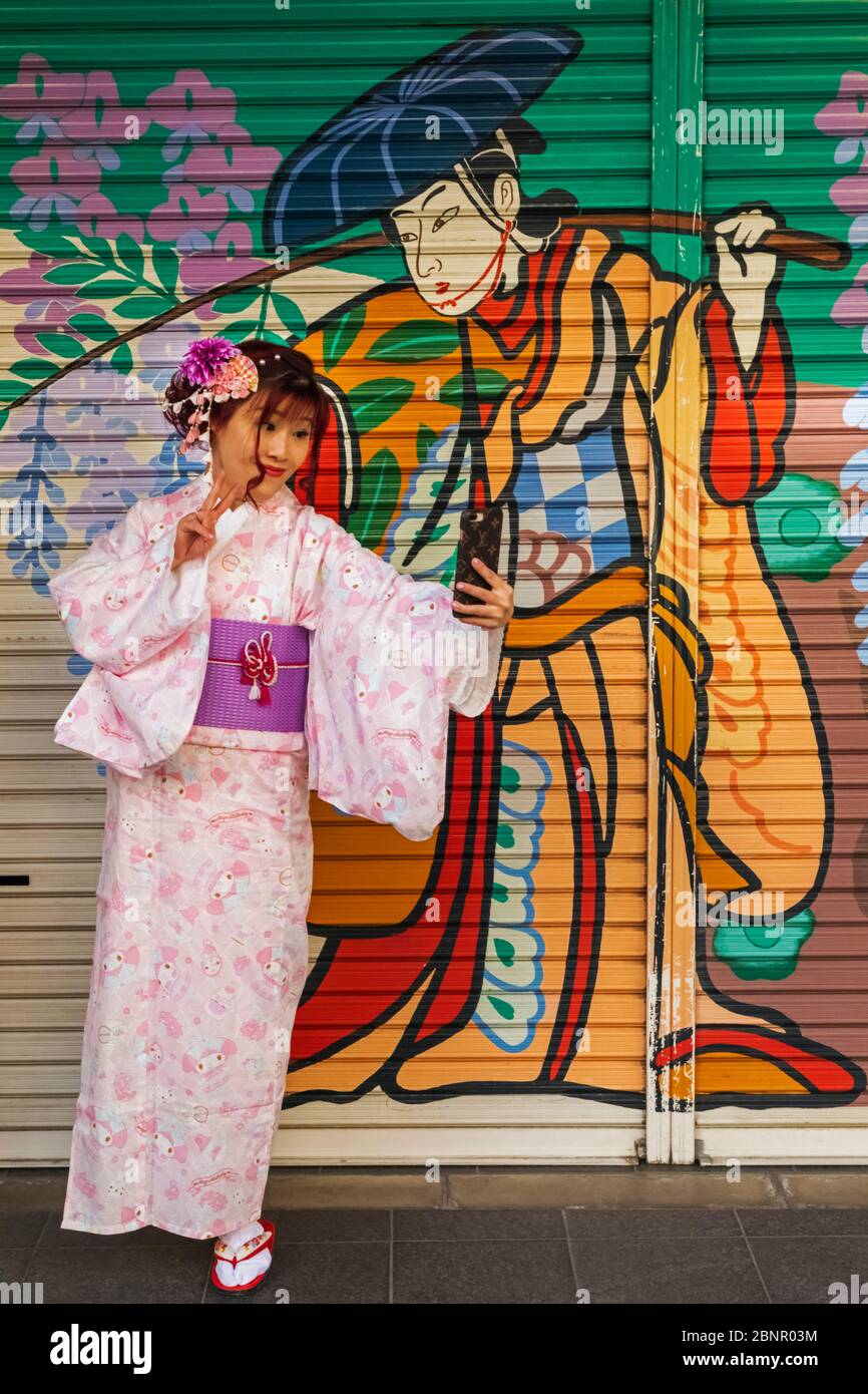 Japón, Honshu, Tokio, Asakusa, Mujer En Kimono Tomando Selfie Fotos Frente A La Colorida Tienda De Pintura Obturador Foto de stock